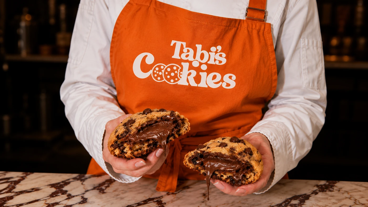 Delantal naranja con el logotipo de Tabi's Cookies y una galleta rellena de chocolate partida a la mitad